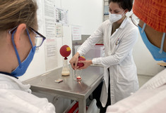 Vortragende demonstriert einen Versuch wo Gas aus einem Ballon in ein Glas mit einer Kerze eingebracht wird