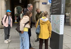 Several people are standing in a pedestrian zone in front of an information board with a city map.