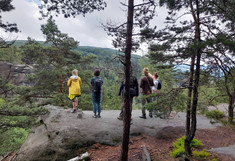 Several people, photographed from behind, stand on the upper edge of the rock and look into the beautiful landscape.