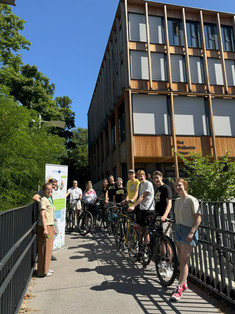 Auf dem Foto sind 11 Personen vor einem Holzhaus (Ilse-Wallentin-Haus) zu sehen. Acht von ihnen stehen mit Fahrrädern. Außerdem ist ein Poster des Projekts Greenpath im Bild zu erkennen.