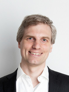 Portraitfoto von Markus Drapalik lächelnd mit weißem Hembt und schwarzem Sako