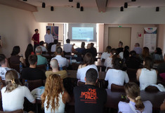 Blick von hinten in einen voll besetzten Seminarraum während der offiziellen Eröffnungszeremonie des Workshops in Belgrad. Auf einer großen Projektionsfläche an der Stirnseite ist die Titelfolie der Präsentation „City and Traffic“ zu sehen, während zwei Vortragende daneben stehen.