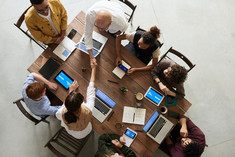 Menschen an einem Tisch mit Laptops und Smartphones reichen sich die Hände