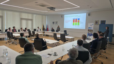 Eine Präsentation im Rahmen der SUM-Foren 2026 in einem hellen Konferenzraum. Sandra Wegener steht vorne am Rednerpult und hält einen Vortrag vor einem Auditorium mit zahlreichen Teilnehmerinnen und Teilnehmern, während im Hintergrund Diagramme an die Leinwand projiziert werden.