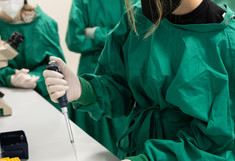 Teilnehmerin in grüner Schutzkleidung pipettiert eine Flüssigkeit in ein Reaktionsgefäß