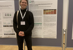 Dressed entirely in black, Fridtjof Diekmann stands smiling in front of his poster.