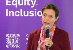 Stefanie Lemke mit einem Mikrophon vor dem Rollup der Koordinationsstelle beim Vorstellen ihrer Lehrveranstaltung.