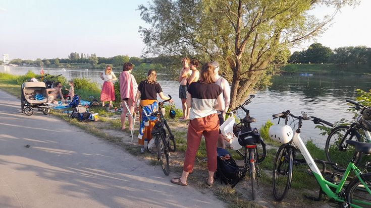 Foto: Einige Personen mit Fahrrädern im Vordergrund, dahinter die neue Donau.