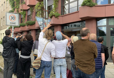 Twelve people (with their backs to the viewer) are looking at the facade greenery of a multi-story house.