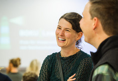 Zwei Personen, die lachen, im Hintergrund die Leinwand mit dem Logo des Projekts