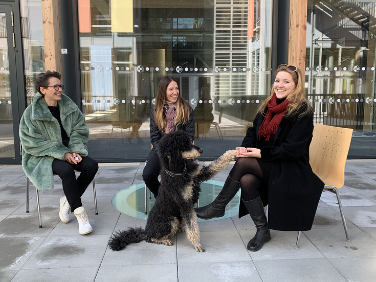 v.l.n.r Ela Posch, Ruth Scheiber-Herzog und Helene Steiner sitzen vor dem Ilse Wallentin Haus auf Stühlen. in der Mitte sitzt Ruth's Königspudel Frida und gibt Helene die Pfote