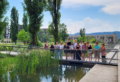 Studierende auf einer Brücke über einem naturnahen künstlichen Teich.