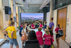 Eine Gruppe von kleinen Kindern und Karl Bittner um einen Tisch mit Tischprojektion -- im Hintergrund die LED Wall. 