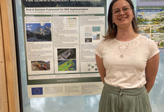 A female scientist stands in front of her poster and smiles at the camera.