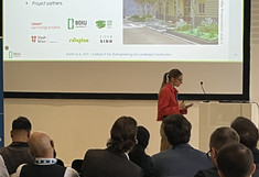 Speaker Anna Briefer in a red jacket, some listeners from behind, the presentation in the background.