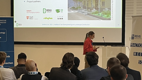 Speaker Anna Briefer in a red jacket, some listeners from behind, the presentation in the background.