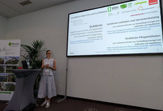 Anna Briefer vor dem Rednerpult, seitlich ihre Präsentation am großen Monitor