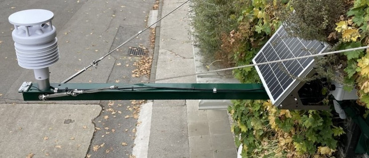 Wetterstation an der Fassadenbegrünung von oben fotografiert. Das Solarpanel ist nahe an der Begrünung befestigt, das Pyranometer mit einer Metallkonstruktion und Spanndrahtseilen in 1,5m Entfernung daran.