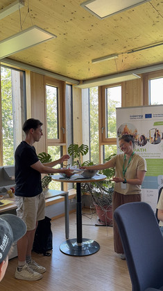 Auf dem Foto sind zwei Personen in einem Raum zu sehen: Eine Frau (Valerie Jeepjua) überreicht einem Studenten einen Preis. Im Hintergrund steht ein Banner des Projekts Greenpath.