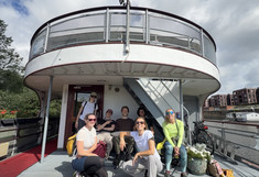 7 people on a small ship look into the camera in a good mood