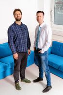 A photo of the two researchers standing in front of blue sofas.