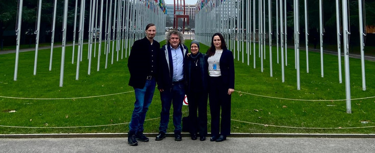 Fahnenallee der Vereinten Nationen mit Blick auf das Landminen-Denkmal „Broken Chair“ am Place des Nations. Personen v.l.n.r.: Johannes Frieß, Gunnar Jeremias, Dunja Sabra, Ana Romeral. Foto mit freundlicher Genehmigung eines anonymen Passanten