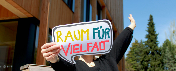 Eine Person hält ein Schild mit der Aufschrift "Raum für Vielfalt" ins Bild